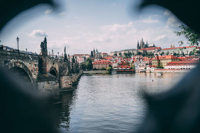 Bridge over river by buildings in city against sky