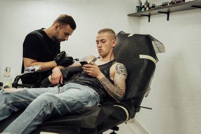 Tattooed man on the process of creating new tattoo at studio, male artist draws on the client skin	
