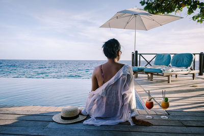 Rear view of woman sitting pier near sea