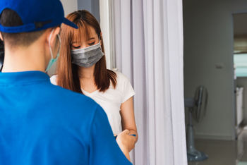 Young woman wearing mask taking delivery standing at door