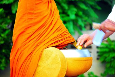 Midsection of monk wearing orange traditional clothing outdoors