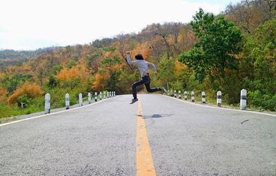 Full length of man jumping on road amidst trees