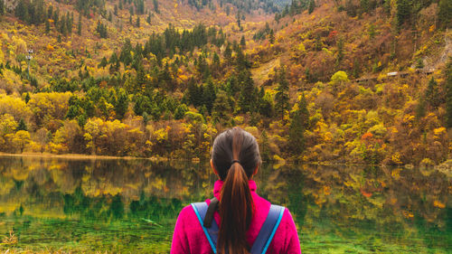 Rear view of woman standing by lake with reflection of trees during autumn