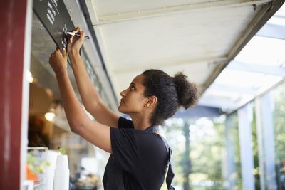 Side view of young waitress writing on menu at cafe