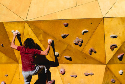 Rear view of woman climbing on yellow wall