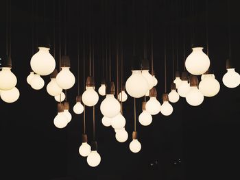 Illuminated light bulbs hanging against black background