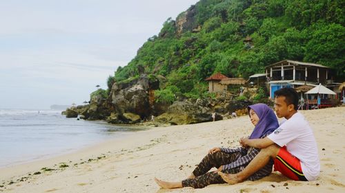 Side view of young man sitting at beach