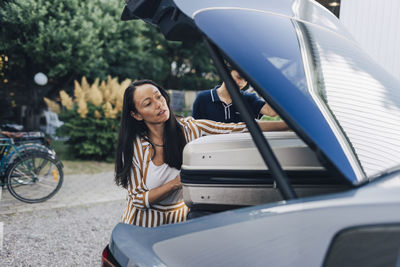 Mature woman with long hair loading luggage in car trunk