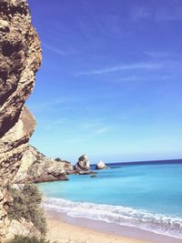 Sea by rock formations against blue sky