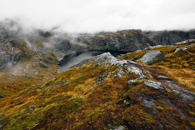 Hiking man at cliff edge with scenic view of lake and mountains at munkebu in lofoten norway