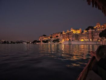 Illuminated buildings by river against clear sky at night