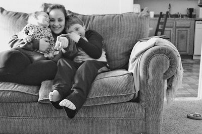 Portrait of mother gesturing sitting with children on sofa at home