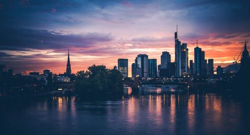 Scenic view of river by buildings against sky during sunset