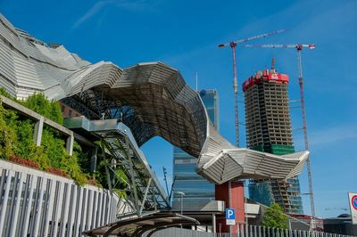 Low angle view of crane by building against blue sky