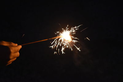 Cropped hand holding illuminated sparkler at night