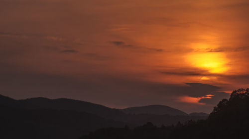 Scenic view of dramatic sky over silhouette mountains during sunset