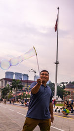 Young man with bubble wand against sky