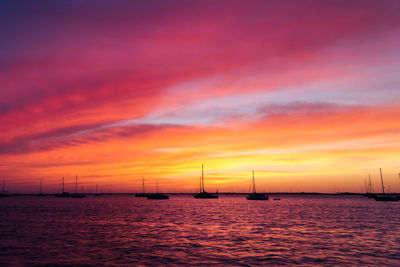 Silhouette sailboats in sea against dramatic sky during sunset