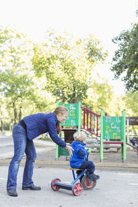 Full length of teacher pushing boy riding tricycle