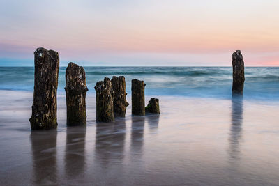 Wooden posts in sea against sky during sunset