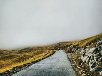 Road amidst landscape against sky during foggy weather