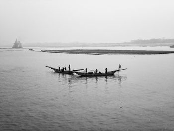 Silhouette fishermen on boats in lake against clear sky