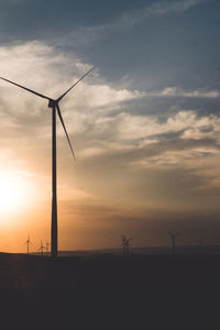 Silhouette wind turbines on field against sky during sunset