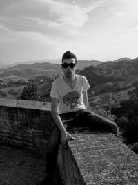 Portrait of young man sitting on mountain against sky