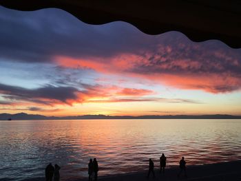 Silhouette people on beach against sky during sunset