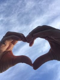 Low angle view of hands making heart shape against sky