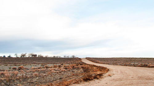 Dirt road amidst field against sky