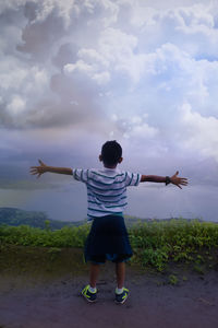 Rear view of man with arms outstretched standing against sky