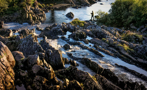 The angler stands attentively in the evening sun in the rocky rugged landscape by the wild water