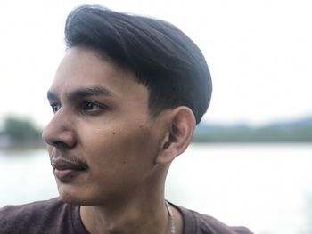 Close-up portrait of young man looking away against sky