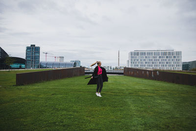 Woman walking on field against sky in city