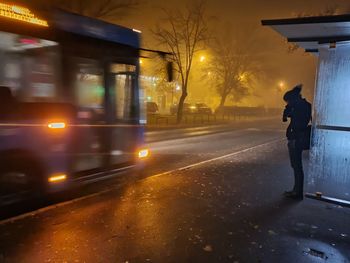 Rear view of person on illuminated street during rainy season at night