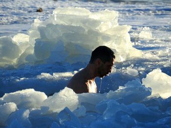 Side view of shirtless man swimming in frozen river