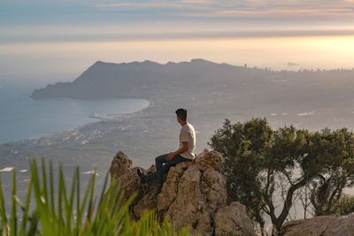 Woman sitting on rock looking at mountain against sky