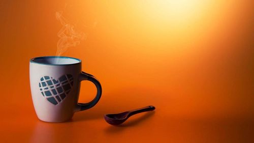 Close-up of coffee cup against orange background