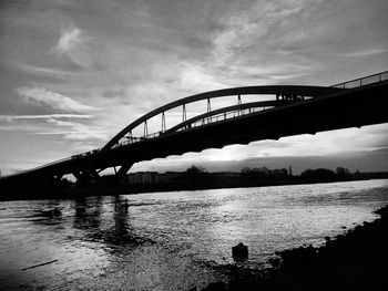 Silhouette bridge over river against sky