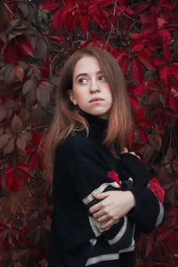 Autumn portrait of a beautiful cute woman against a background of bright red leaves. black sweater