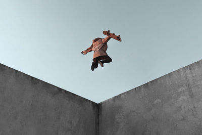 From below full body back view of young skater in casual clothes with skateboard jumping on concrete ramp in skate park performing trick