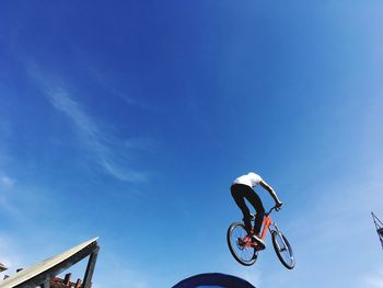 Low angle view of man with bicycle against blue sky