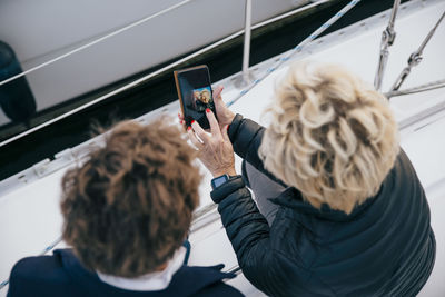 High angle view of senior woman showing photograph on mobile phone to female friend in yacht