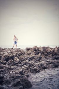 Man standing on rock by sea against clear sky