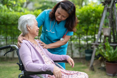 Doctor caregiver help and care asian senior woman patient sitting on wheelchair in park