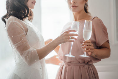 Midsection of bridesmaid and bride holding champagne flute