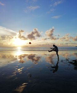 Silhouette person with ball on beach against sky during sunset