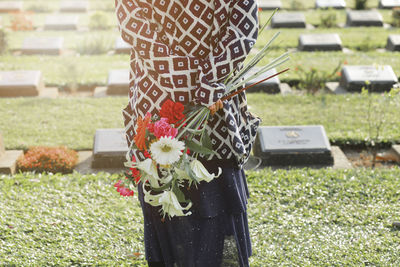 Midsection of woman holding flower standing in cemetery