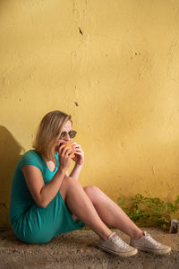 Young woman sitting against wall